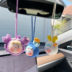 Puede incluir: Tres adornos de animales del zod&iacute;aco hechos a crochet colgando del espejo retrovisor de un coche. Los adornos son un cangrejo morado, un pez azul y un carnero blanco.