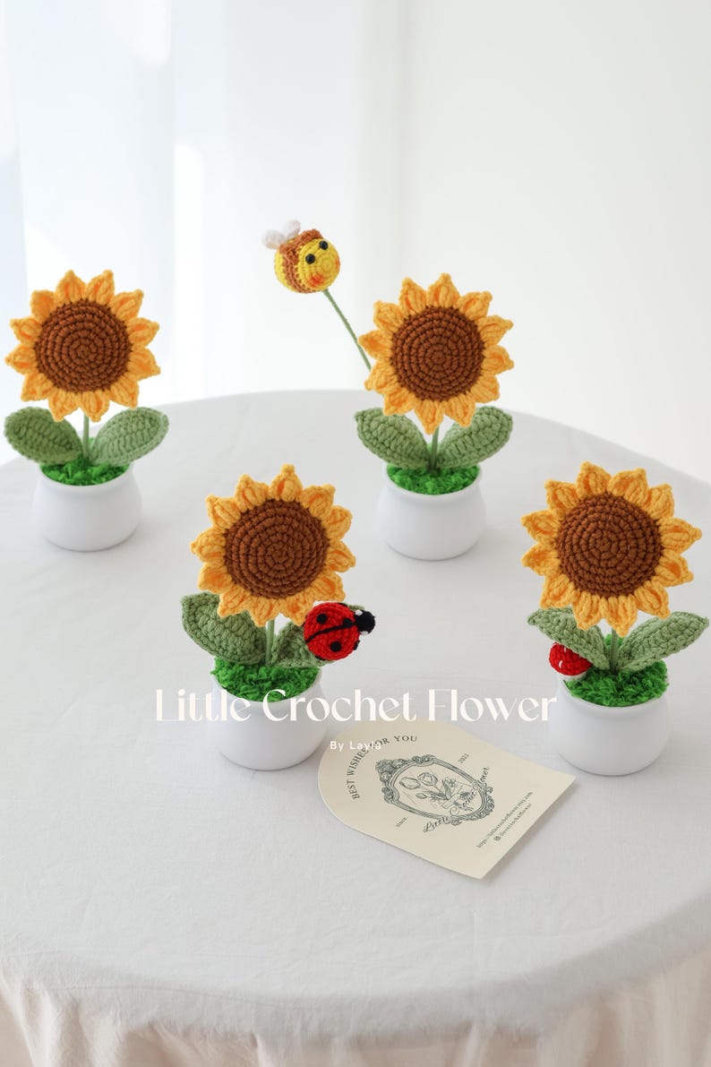 May include: Crocheted sunflowers in white pots with green leaves and brown centers. A crocheted bee and ladybugs accent the flowers. The text "Little Crochet Flower" is visible.
