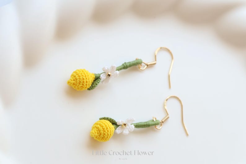 Puede incluir: Un par de pendientes de lim&oacute;n hechos a crochet con detalles de flores blancas y ganchos dorados. Los pendientes son hechos a mano y tienen un dise&ntilde;o delicado.