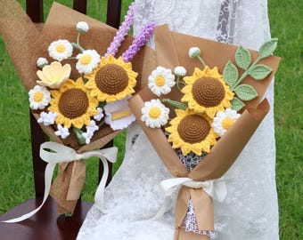 Puede incluir: Dos ramos de flores de ganchillo envueltos en papel marrón y atados con cintas blancas. Los arreglos incluyen girasoles amarillos con centros marrones, margaritas blancas con centros amarillos, hojas verdes y tallos de color púrpura.
