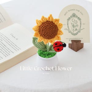 May include: A handmade crochet sunflower with a ladybug accent in a white pot. The sunflower has yellow petals and a brown center. The ladybug is red with black spots. The text "Little Crochet Flower" is at the bottom.