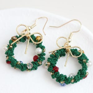 May include: A pair of green Christmas wreath earrings with gold hooks and a gold bow. The wreaths are decorated with red, white, and blue beads.