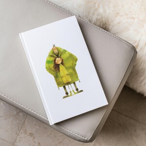 May include: A watercolour illustration of a man and a girl wearing matching green and yellow raincoats. The illustration is printed on a white notebook.