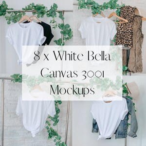 May include: Eight white Bella Canvas 3001 t-shirts on hangers, displayed against a white tiled wall with greenery. The t-shirts are blank and ready for customisation.