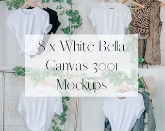 May include: Eight white Bella Canvas 3001 t-shirts on hangers, displayed against a white tiled wall with greenery. The t-shirts are blank and ready for customization.