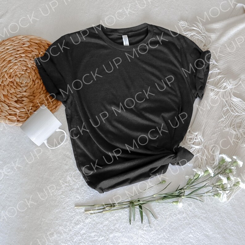 May include: A black t-shirt with a crew neck and short sleeves, laid flat on a white surface with a wicker coaster, a white mug, and a bouquet of white flowers.