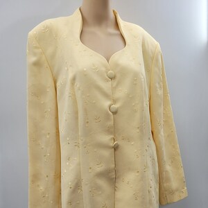 May include: A pale yellow suit with a skirt and jacket. The fabric has a delicate floral embroidery pattern.