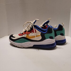 Pode incluir: Par de tênis Nike Air Max 270 React. Os sapatos apresentam uma base branca com detalhes coloridos em vermelho, laranja, amarelo, verde e azul. As solas são brancas com um calcanhar azul e preto.