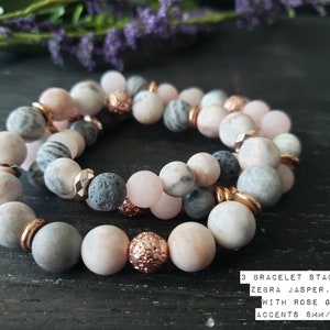 May include: Three-strand bracelet stack featuring pink zebra jasper, lava rock beads, and rose gold accents. The beads are 8mm and 10mm in size.
