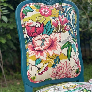 Pode incluir: Cadeira pintada de azul turquesa com um assento de tecido com padr&atilde;o floral. O tecido apresenta uma variedade de flores rosa, vermelhas, amarelas e verdes sobre um fundo branco.