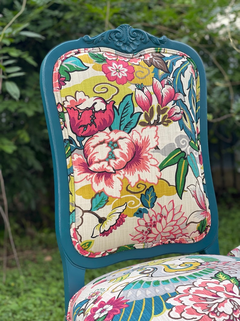 Pode incluir: Cadeira pintada de azul turquesa com um assento de tecido com padr&atilde;o floral. O tecido apresenta uma variedade de flores rosa, vermelhas, amarelas e verdes sobre um fundo branco.
