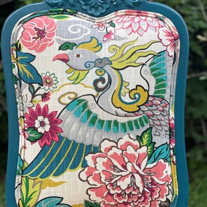 Pode incluir: Cadeira azul turquesa com um assento de tecido estampado com flores que apresenta um design de p&aacute;ssaro colorido. A cadeira tem uma parte superior de madeira esculpida e um encosto curvo.