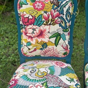 Pode incluir: Cadeira de jantar azul turquesa com assento e encosto de tecido com padr&atilde;o floral. O tecido apresenta uma grande flor rosa, folhas verdes e um design de p&aacute;ssaro amarelo e cinza.