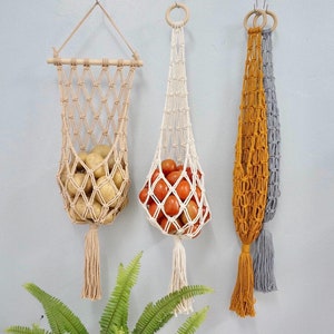 May include: Three macrame hanging baskets with wooden dowels and tassels. The baskets are filled with potatoes, tomatoes, and are empty.