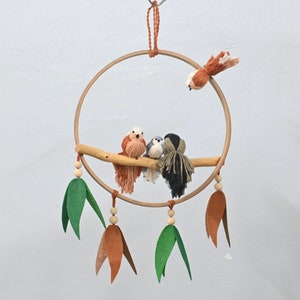 Könnte beinhalten: Ein Holzreifen mit einem Ast und vier Wollvögeln, die daran hängen. Der Reifen hat grüne und braune Filzblätter, die daran hängen. An der Schnur, die die Blätter hält, befinden sich Holzperlen.