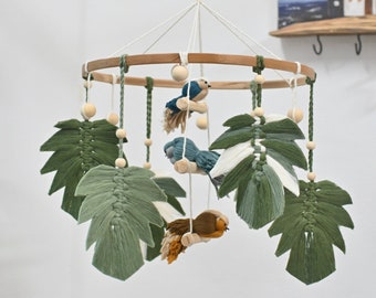 May include: A wooden baby mobile with green and white leaves, blue birds, and a brown bird. The mobile is hanging from a white ceiling hook.