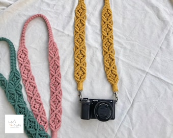 May include: Three macrame camera straps in mustard yellow, dusty pink, and sage green, each featuring a complex knotted diamond pattern. The mustard yellow strap is attached to a black Sony camera with metal swivel clips at both ends.