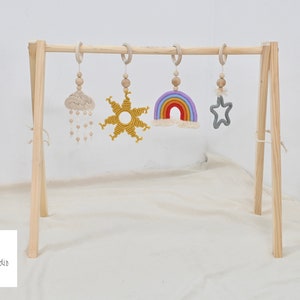 May include: Wooden baby play gym with hanging toys. The toys include a rainbow, a star, a sun, and a cloud with raindrops.