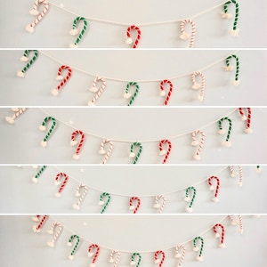 May include: A Christmas garland with multiple strands of candy cane decorations. The candy canes alternate between red and white stripes and green and white stripes, with a fluffy white pom-pom at the end of each. The garland is strung on a white cord.