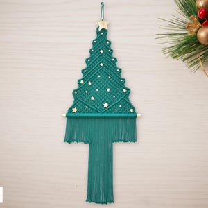 May include: Teal macrame Christmas tree wall hanging with gold star accents. The tree is made with a knotting technique and has a fringe at the bottom.
