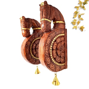 Peut inclure: Deux décorations murales en bois sculpté représentant des têtes de chevaux. Les chevaux sont bruns avec des accents dorés et sont fixés à une base circulaire avec des sculptures détaillées. Chaque pièce a une petite cloche dorée suspendue.