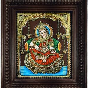 May include: A framed, colorful painting of a seated deity. The figure wears ornate gold jewelry and a red and gold garment. The background is brown with gold accents, and the frame is dark brown.