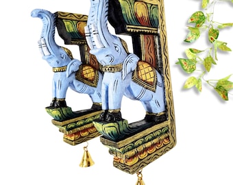May include: Two hand-carved wooden elephant wall shelves. The elephants are painted light blue with gold and black accents. Each shelf has a gold bell hanging from the bottom. The shelves are decorated with colorful patterns.