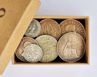 May include: A collection of vintage British coins housed in a small, rectangular, light brown cardboard box. The coins include various denominations such as a 1966 sixpence, a half penny featuring a ship, and pennies depicting Queen Elizabeth II.