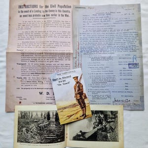 May include: A selection of historical documents, including instructions for the civil population, a medical report, and a propaganda card featuring a soldier. The items are displayed on a light surface, suggesting a glimpse into the past. Measurements are not applicable.