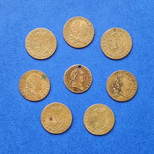May include: A collection of eight gold-colored coins with different designs and dates. The coins feature portraits of a king and a queen, as well as coats of arms.