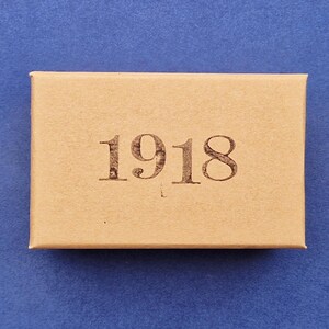 May include: A rectangular, light brown box with the year "1918" printed in a dark brown font. The box is centered on a blue background.