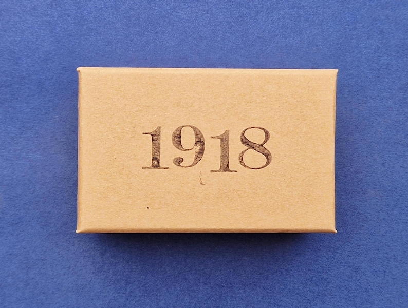 May include: A rectangular, light brown box with the year "1918" printed in a dark brown font. The box is centered on a blue background.