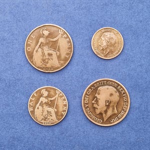 May include: Four antique British coins on a blue background. Two larger coins show a seated woman, with the text "ONE PENNY" and "HALF PENNY". The other two coins feature a profile of a man.