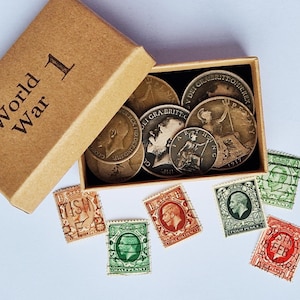 May include: A brown cardboard box labelled World War 1 containing several vintage British coins, including a 1917 farthing. Scattered around the box are six postage stamps in various colours, featuring portraits of King George V and numerical values.