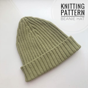 May include: A green knitted beanie hat.  KNITTING PATTERN BEANIE HAT is written in black text above the hat.