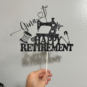 May include: Black glitter cake topper with a sewing machine, spool of thread, and safety pin. The topper says "Gina" and "Happy Retirement".