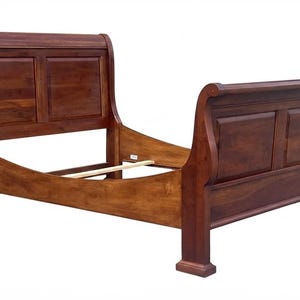 May include: A wooden sleigh bed frame with a rich, medium-brown finish. The design features a tall, curved headboard and a matching lower footboard, both with recessed rectangular panels. The side rails connect the headboard and footboard.