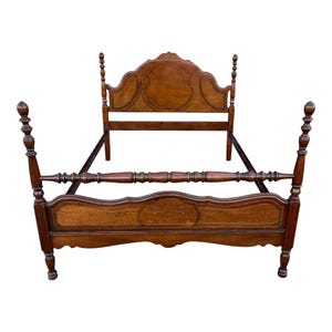 May include: A wooden bed frame with a headboard and footboard. The headboard and footboard have decorative carved details and a dark brown finish. The bed frame has four tall, turned posts at each corner.