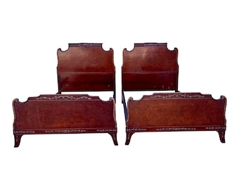 May include: Two antique twin-sized beds with ornate wood headboards and footboards. The beds are made of dark wood with intricate carvings and a reddish-brown finish.