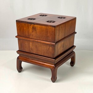 May include: A square wooden box with a rich brown finish, featuring four circular cutouts on the top surface. The box is elevated on a base with four curved legs, showcasing a smooth, polished wood grain texture throughout the entire structure.