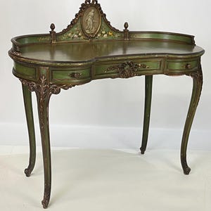 May include: A kidney-shaped vanity desk in a muted green finish with gold-toned accents. It features three drawers, curved cabriole legs, and a raised back gallery with a central oval medallion depicting a figure and hand-painted floral motifs.