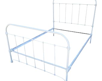 May include: A white metal bed frame with a headboard and footboard. The frame has a classic design with vertical bars and curved accents. The bed frame is empty and ready for a mattress. The bed frame is painted white.