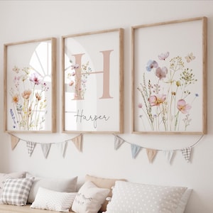 May include: Three framed floral art prints with a light wood finish. The prints feature watercolor flowers in pink, purple, and yellow hues. The center print has a large pink letter "H" and the name "Harper" in script.