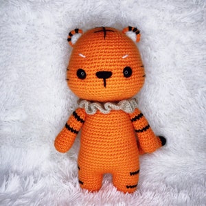 May include: A crocheted orange tiger stuffed animal with black stripes and a white ruffle collar. The tiger has black eyes and a black nose.