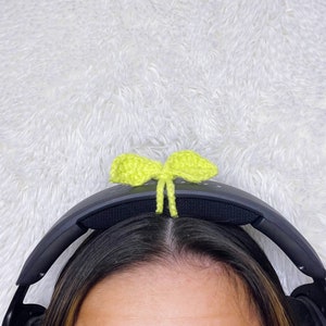 May include: A pair of black headphones with a bright green crocheted bow on the headband.