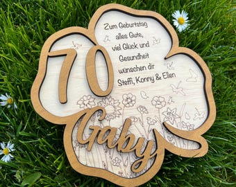 May include: Wooden birthday sign in the shape of a four-leaf clover, with the number 70 in the center. The name "Gaby" is at the bottom, with floral illustrations and German text.