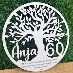 May include: A round, wooden tree of life plaque with the name "Anja" and the number "60" cut out. The plaque has a natural wood finish and includes a message and the name "Birgit" at the bottom.