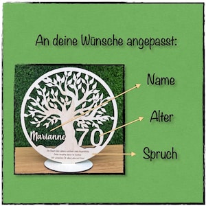 May include: A personalized wooden tree of life decoration. The design features a tree silhouette with the name "Marianne" and the number "70". The text "An deine W&uuml;nsche angepasst" is at the top. The decoration is on a green background.