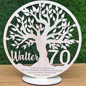 May include: A wooden, laser-cut tree of life design with the name "Walter" and the number "70". The base includes text in German. The tree is set against a green background.