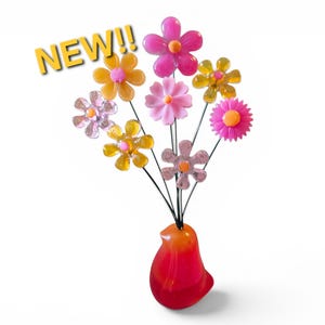 May include: A decorative bird-shaped vase in red and orange, holding a bouquet of eight translucent plastic flowers in shades of pink, yellow, and clear. The flowers are attached to thin black wire stems. The text NEW!! appears in yellow.